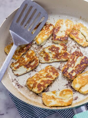Fried halloumi cheese in a ceramic frying pan on a marble background