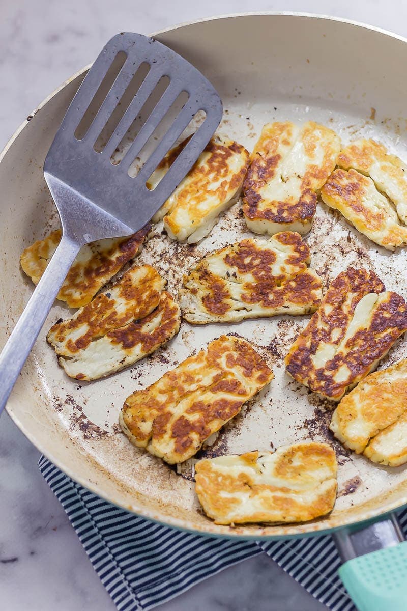 How to cook halloumi. Fried halloumi cheese in a ceramic frying pan on a marble background