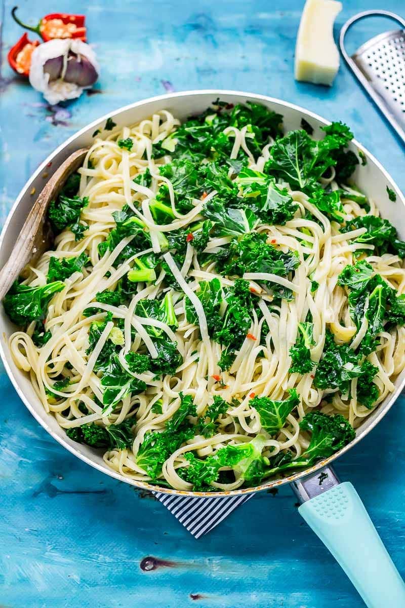 Frying pan of kale pasta with garlic, chilli and parmesan on a blue background