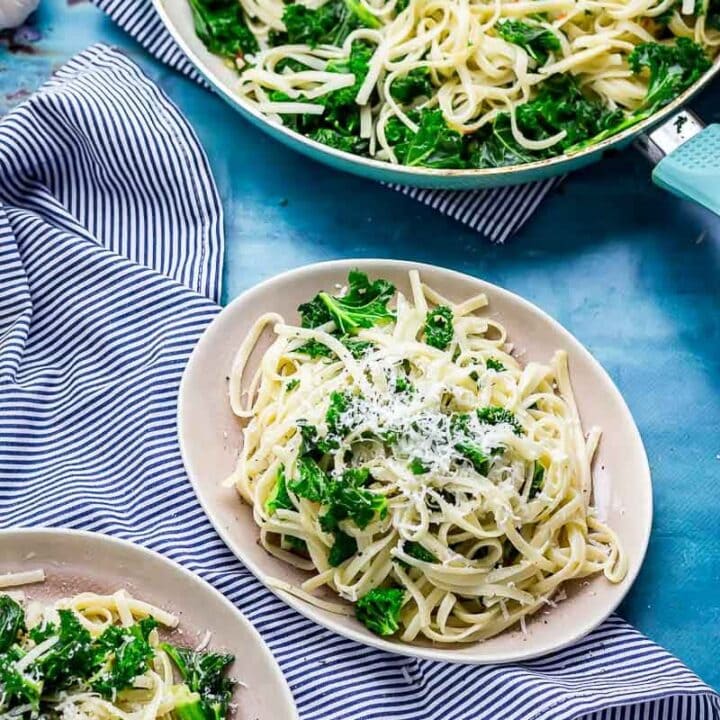 Two plates of kale pasta on a striped cloth and a blue background