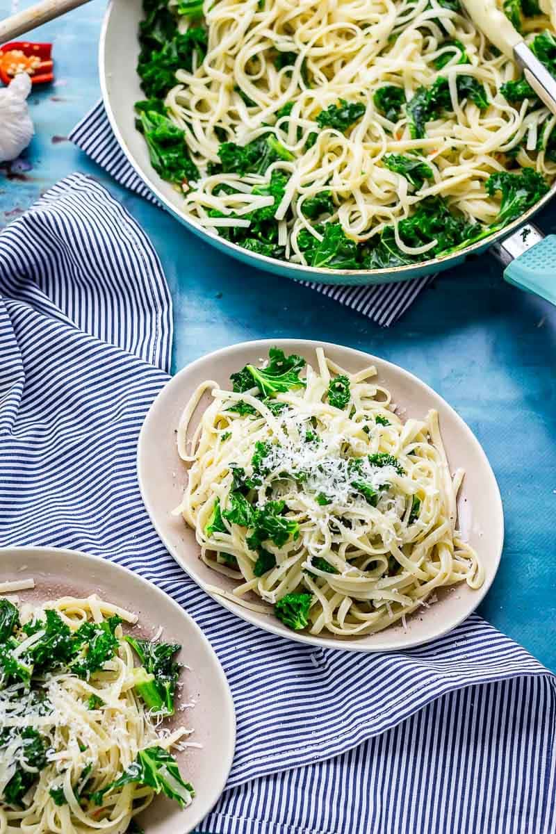 Two plates of kale pasta on a striped cloth and a blue background