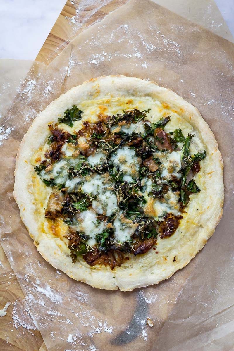 Leftover pulled pork pizza with kale on a wooden board with a marble background