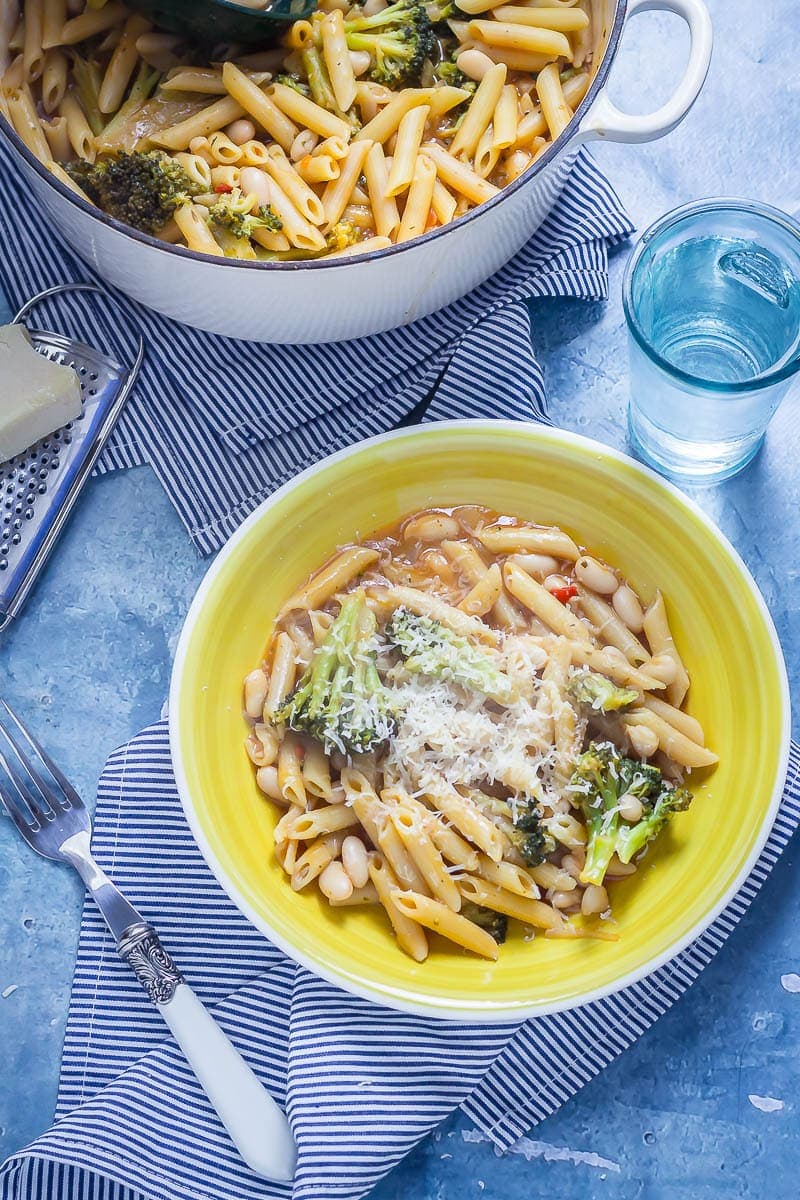 Overhead shot of Broccoli and White Bean One Pot Pasta in a yellow bowl on a striped cloth with a fork