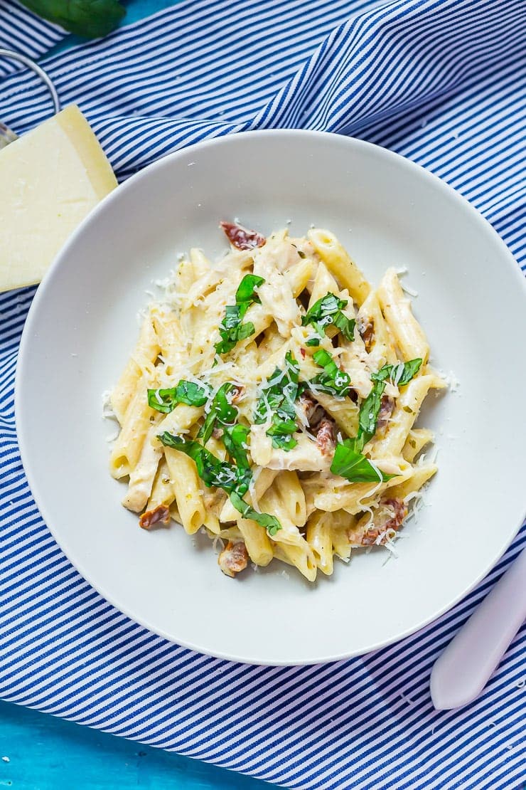 Overhead shot of a bowl of creamy chicken pasta on a striped cloth with a fork and parmesan