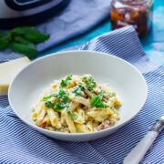 Bowl of creamy chicken pasta on a striped cloth with sun dried tomatoes, parmesan and pressure cooker in the background