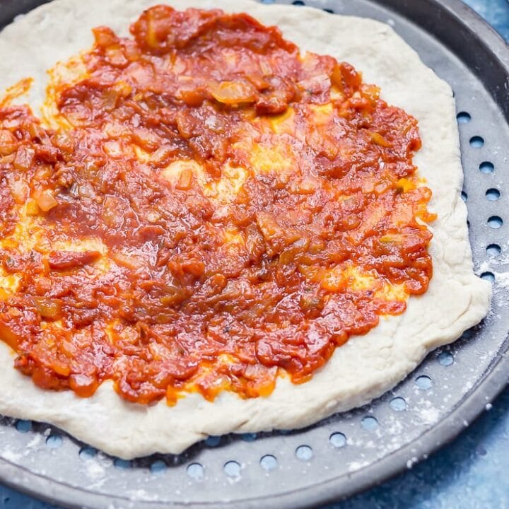 How to make pizza sauce. Homemade pizza sauce on a pizza base on a blue background