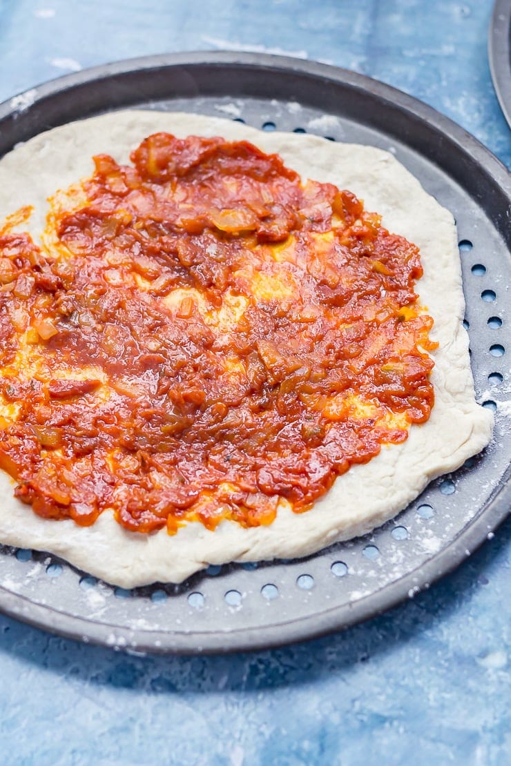 How to make pizza sauce. Homemade pizza sauce on a pizza base on a blue background