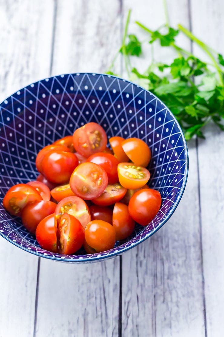 Blue bowl of halved cherry tomatoes on a distressed wooden background