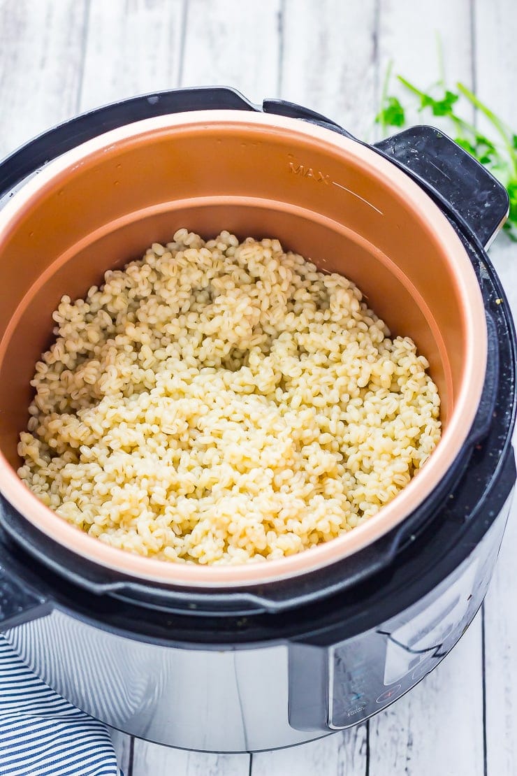 Cooked pearl barley in a pressure cooker on a distressed wood background