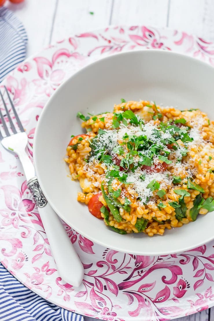 Bowl of One Pot Cheesy Pearl Barley with Tomatoes on a pink platter