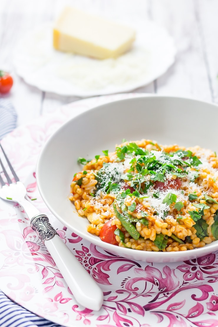 Bowl of One Pot Cheesy Pearl Barley with Tomatoes on a pink platter with parmesan in the background