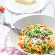 Cheesy pearl barley with tomatoes on a bowl with a fork and parmesan in the background