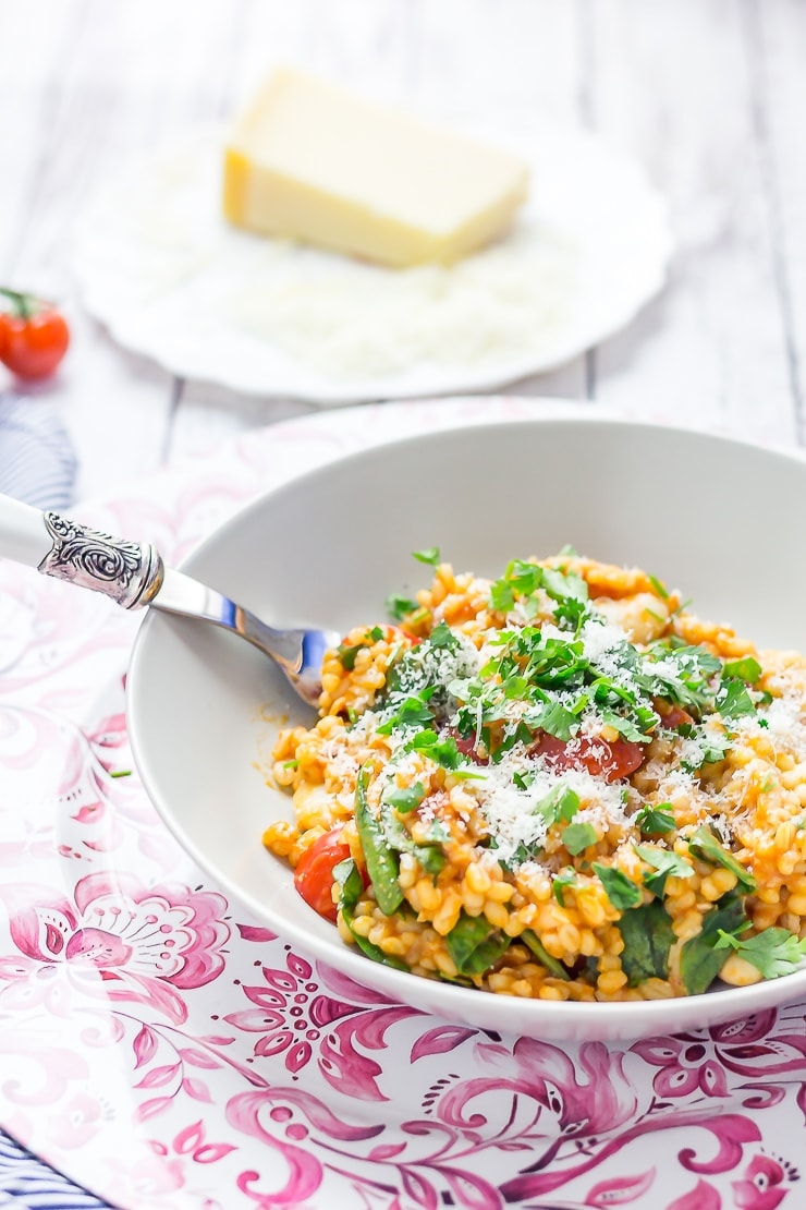 Cheesy pearl barley with tomatoes on a bowl with a fork and parmesan in the background