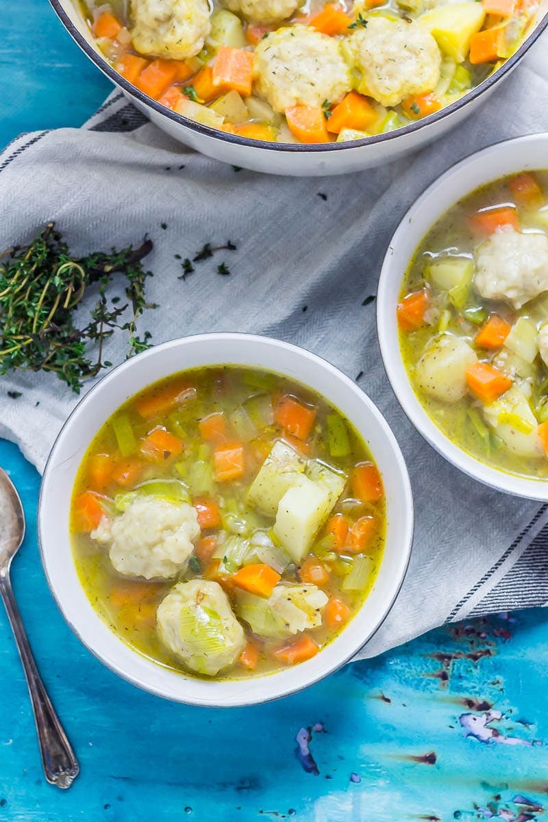 Two bowls of vegetable soup with dumplings on a tea towel on a blue background