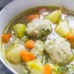 A bowl of Vegetable Soup with Dumplings topped with thyme sprigs
