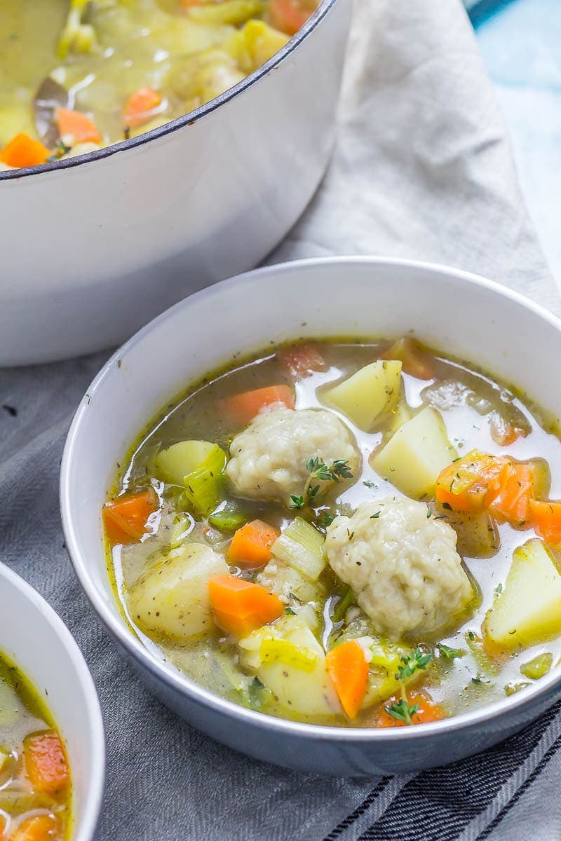 Bowl of vegetable soup with dumplings with a pot of soup in the background