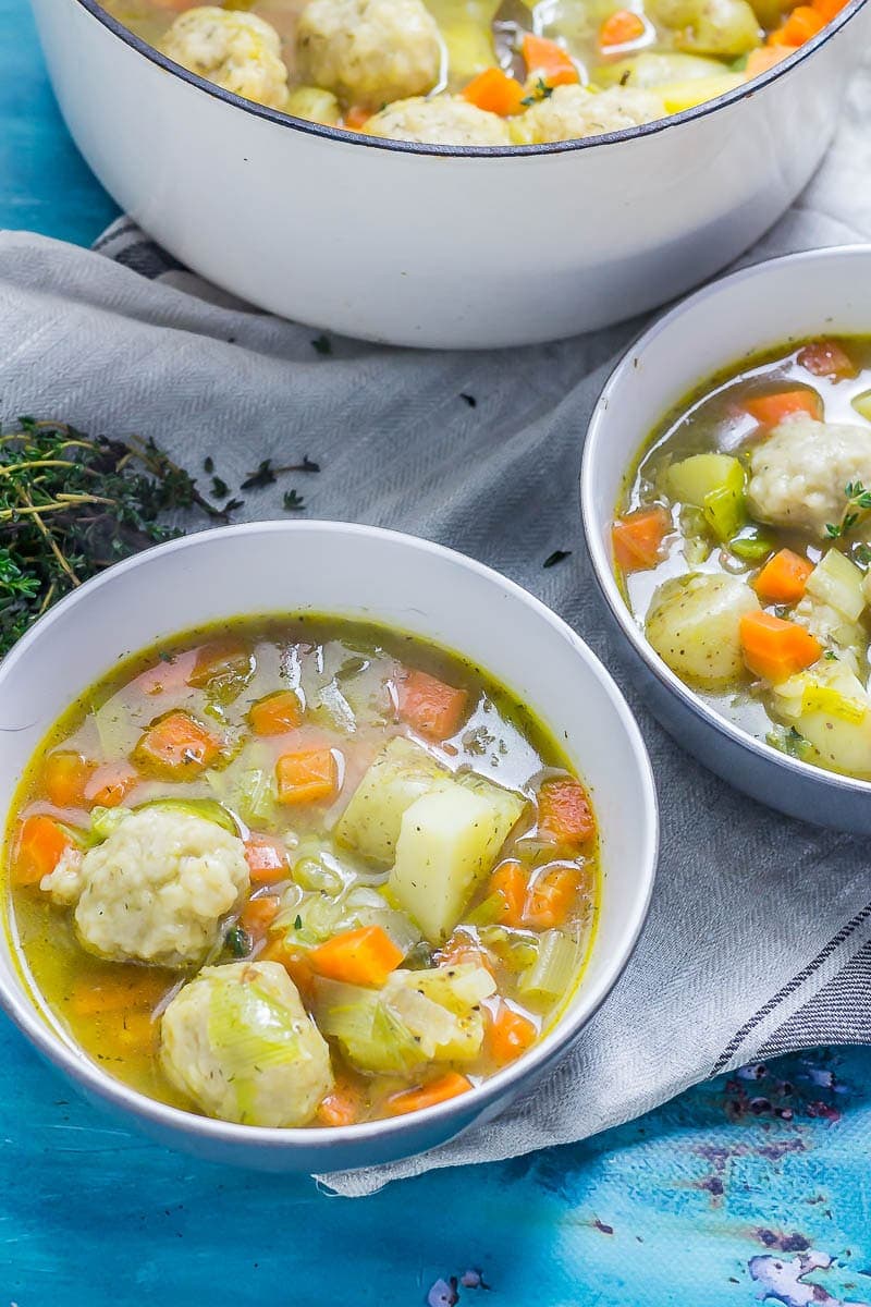 Two bowls of vegetable soup with dumplings with a pot of soup in the background