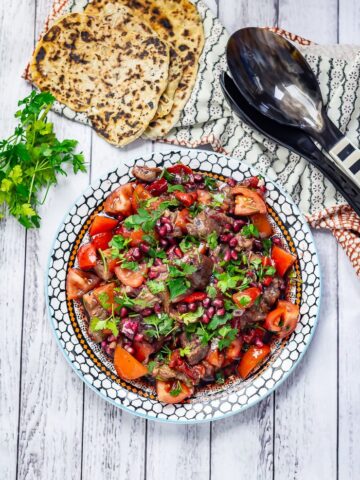 Overhead shot of Smoky Aubergine Salad with Red Pepper on a white wooden background with bread and parsley