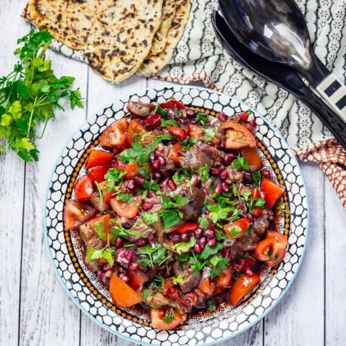 Overhead shot of Smoky Aubergine Salad with Red Pepper on a white wooden background with bread and parsley