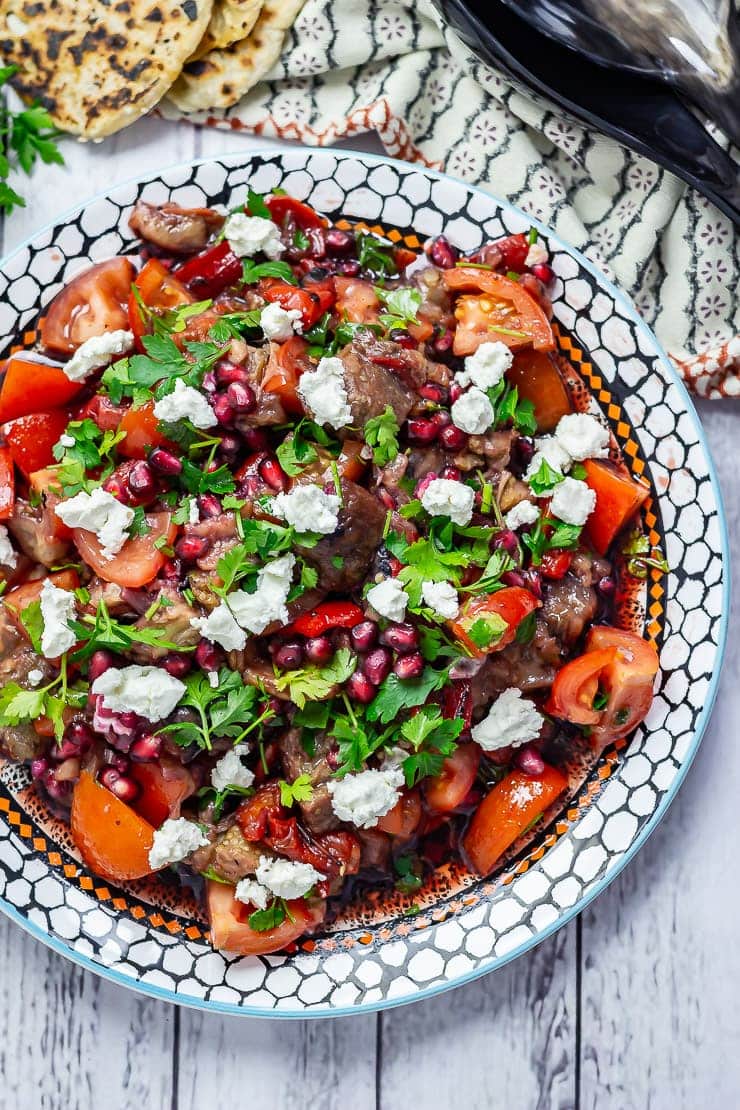 Smoky Aubergine Salad with Red Pepper on a patterned plate on a white wooden background and a patterned cloth.