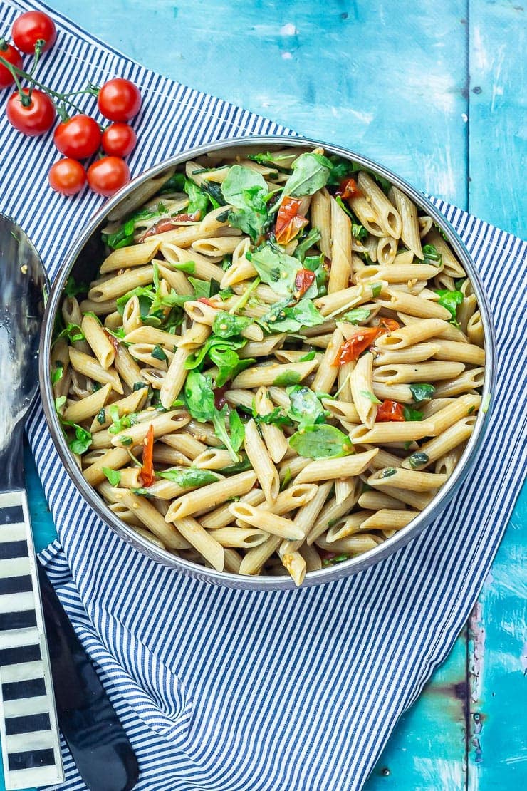 Overhead shot of balsamic pasta salad on a striped cloth with cherry tomatoes and salad servers