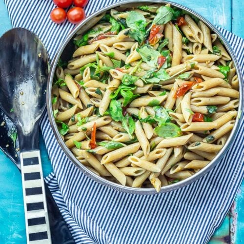 Overhead shot of Simple Pasta Salad with Balsamic on a striped cloth with salad servers and cherry tomatoes
