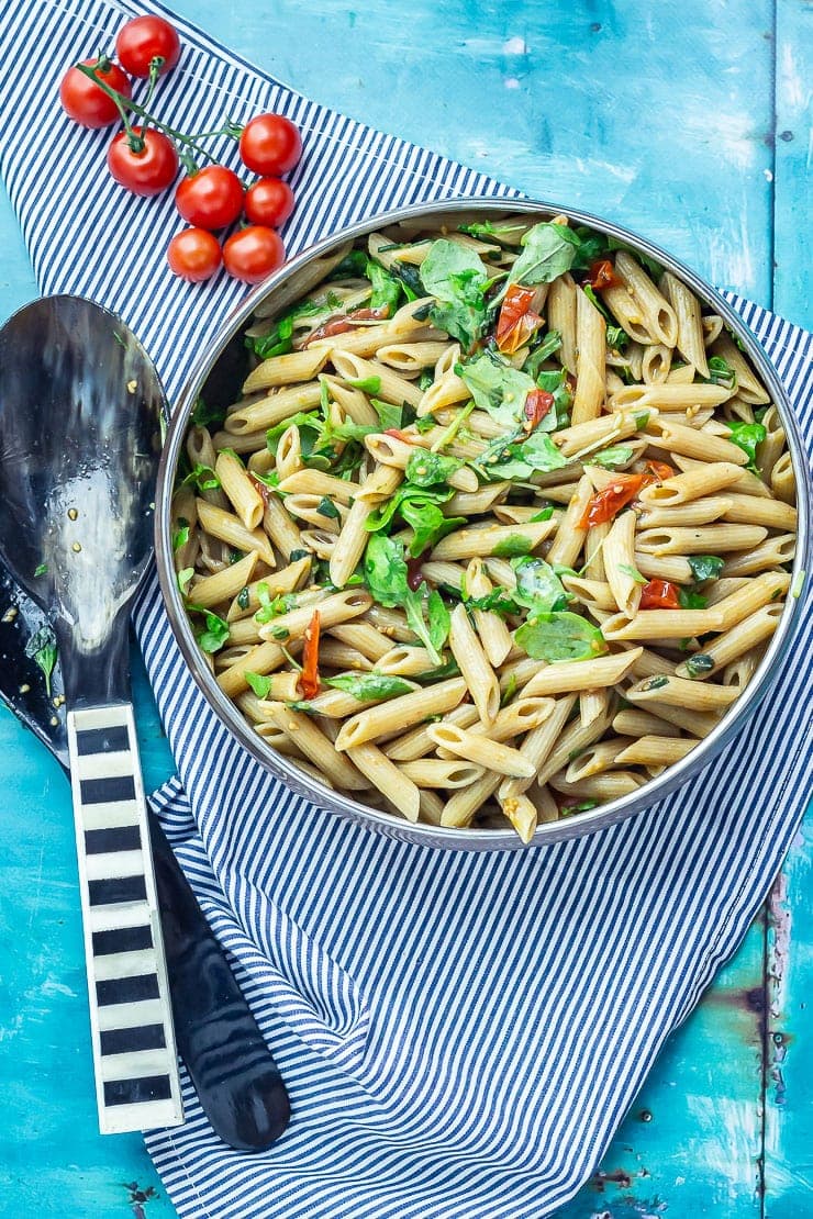 Overhead shot of Simple Pasta Salad with Balsamic on a striped cloth with salad servers and cherry tomatoes