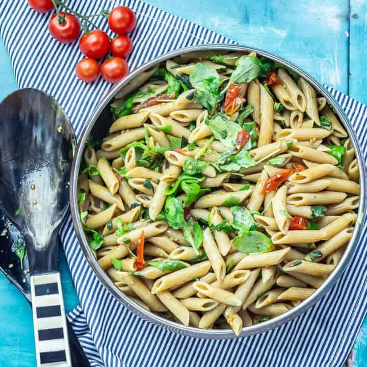 Overhead shot of Simple Pasta Salad with Balsamic on a striped cloth with salad servers and cherry tomatoes