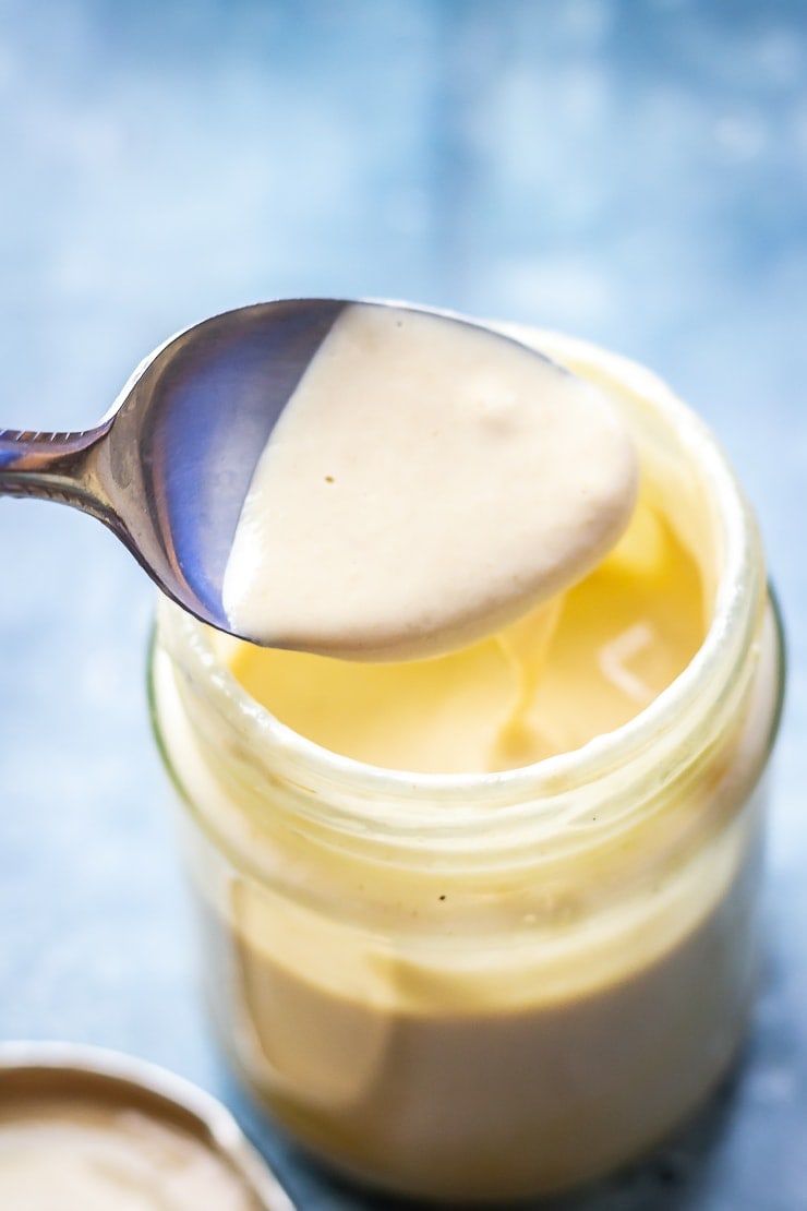 Jar of sesame dressing with a spoon on a blue background