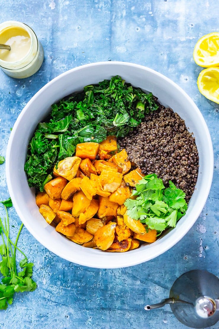 Overhead of Sweet Potato and Quinoa Salad with Sesame Dressing ingredients on a blue background with lemon and dressing 