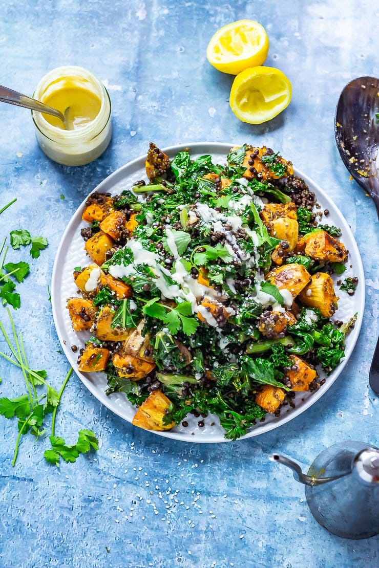 Overhead shot of Sweet Potato and Quinoa Salad with Sesame Dressing on blue background with dressing, lemon and coriander