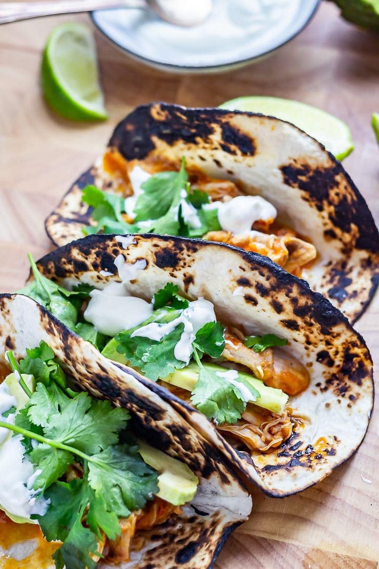 Three chipotle chicken tacos on a wooden board with lime wedges