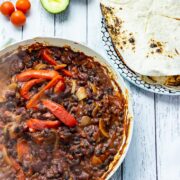 Overhead shot of veggie fajitas with tortillas, avocado and cherry tomatoes on a white wooden background