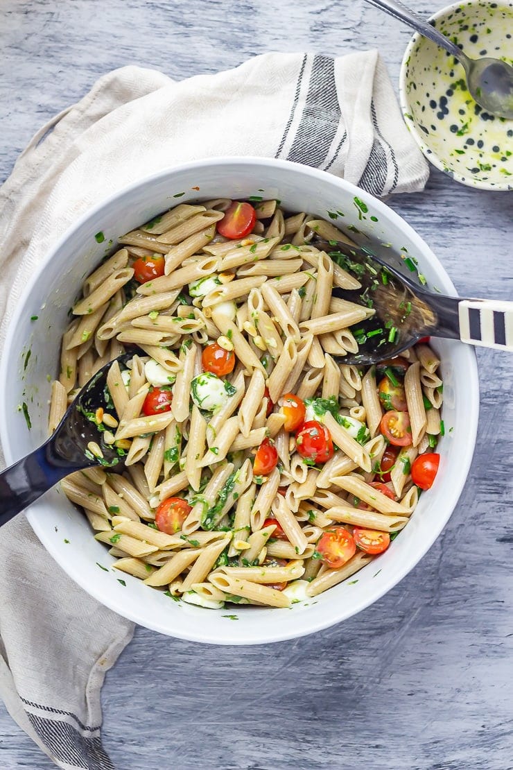 Overhead shot of caprese pasta salad on a grey background with a cloth and basil dressing