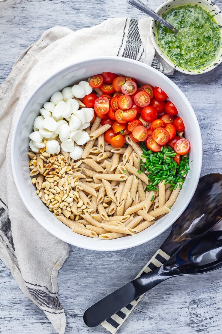 Overhead shot of caprese pasta salad with cloth, salad servers and basil dressing