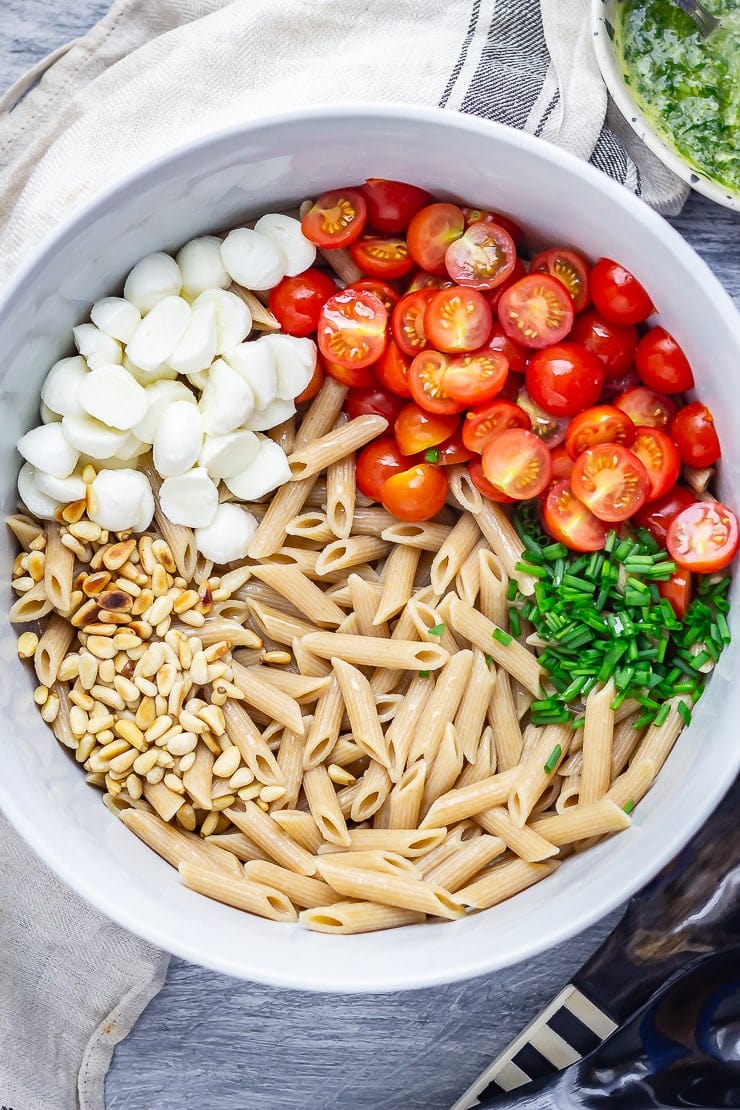 Overhead shot of caprese pasta salad with a cloth on a blue background