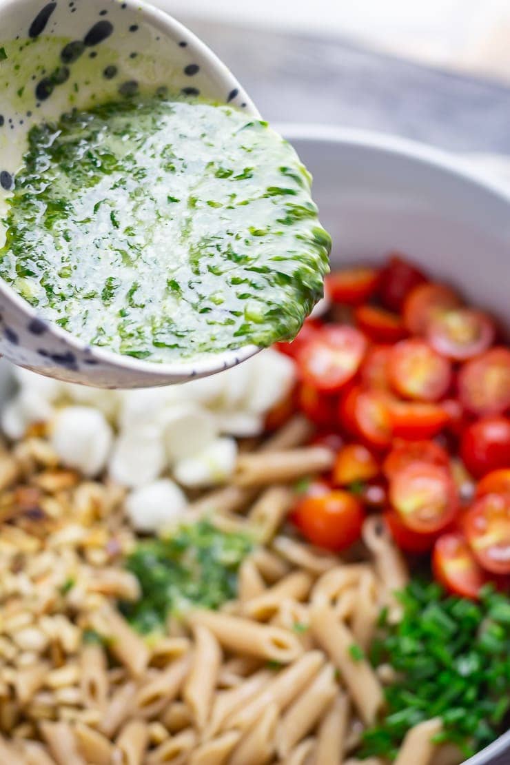 Basil dressing pouring onto caprese pasta salad