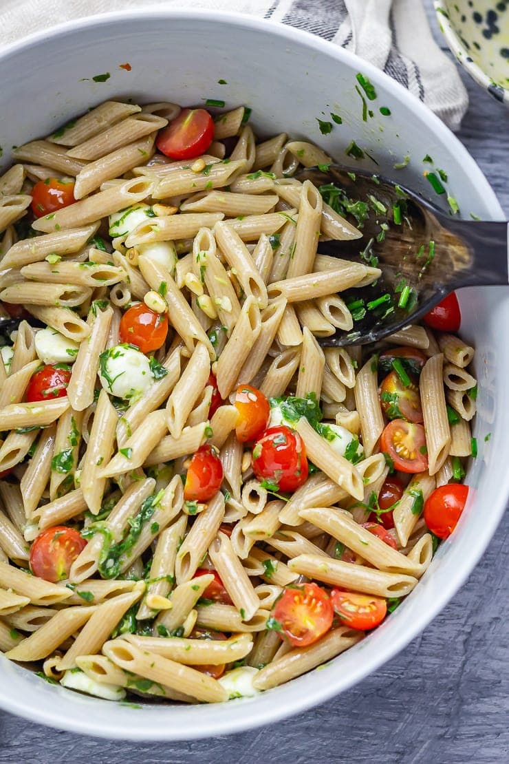 Overhead shot of caprese pasta salad with salad servers