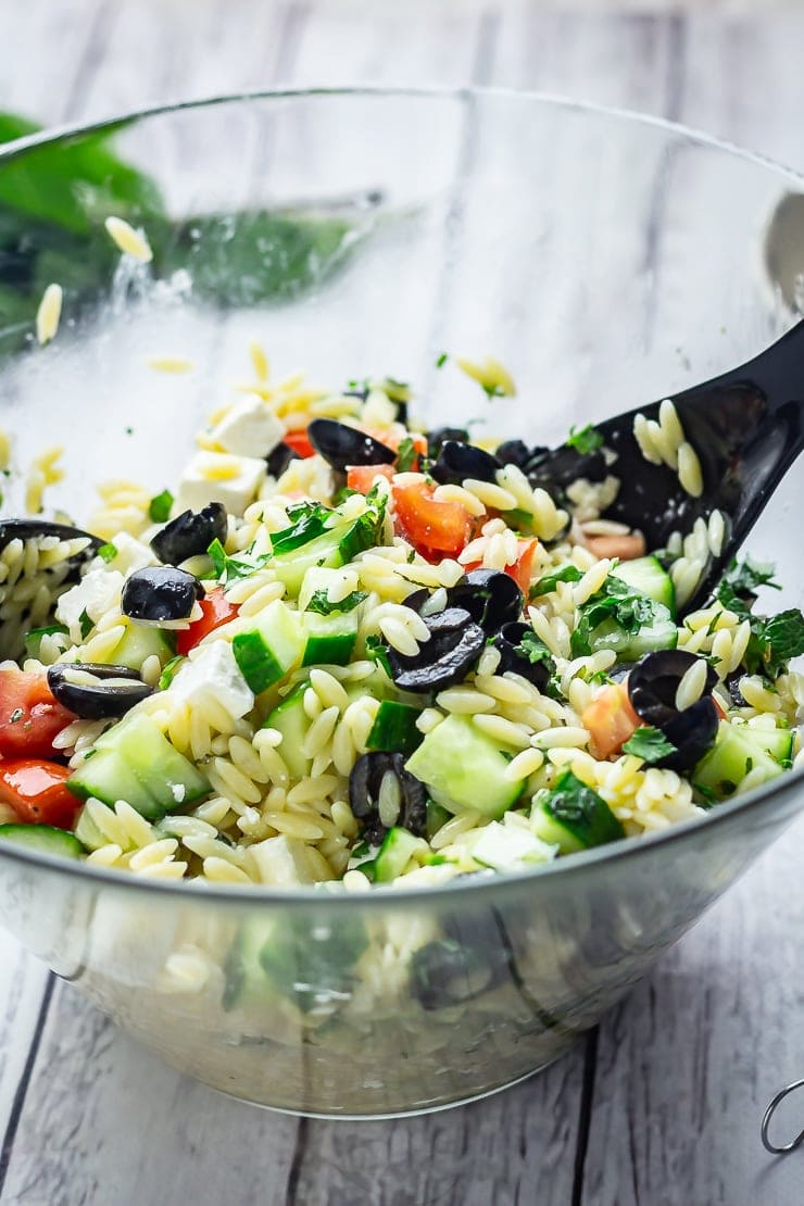 Greek Orzo Salad with Lemon Dressing in a glass bowl on a white wooden background