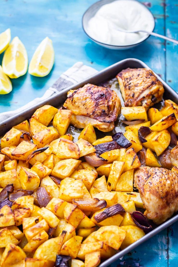 Sheet Pan Harissa Chicken with Potatoes on a blue background with lemon and yoghurt 