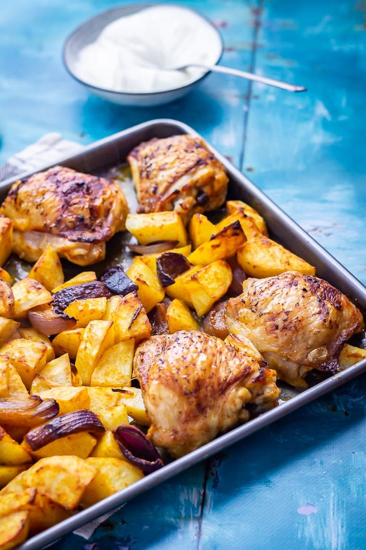 Sheet Pan Harissa Chicken with Potatoes on a blue background with garlic yoghurt