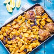 Overhead shot of sheet pan harissa chicken on a blue background with lemon and yoghurt