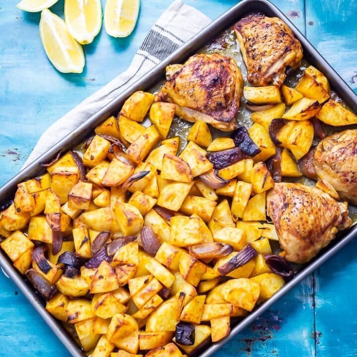 Overhead shot of sheet pan harissa chicken on a blue background with lemon and yoghurt
