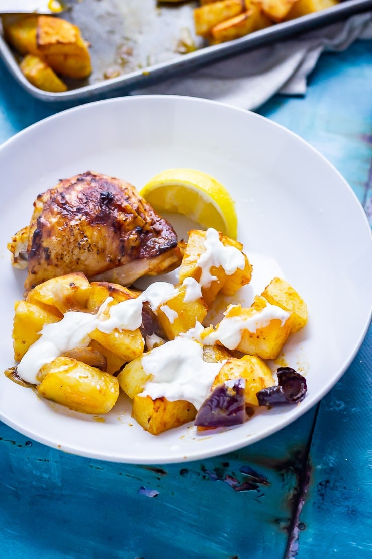 Sheet Pan Harissa Chicken with Potatoes in a white bowl with a lemon slice on a blue background