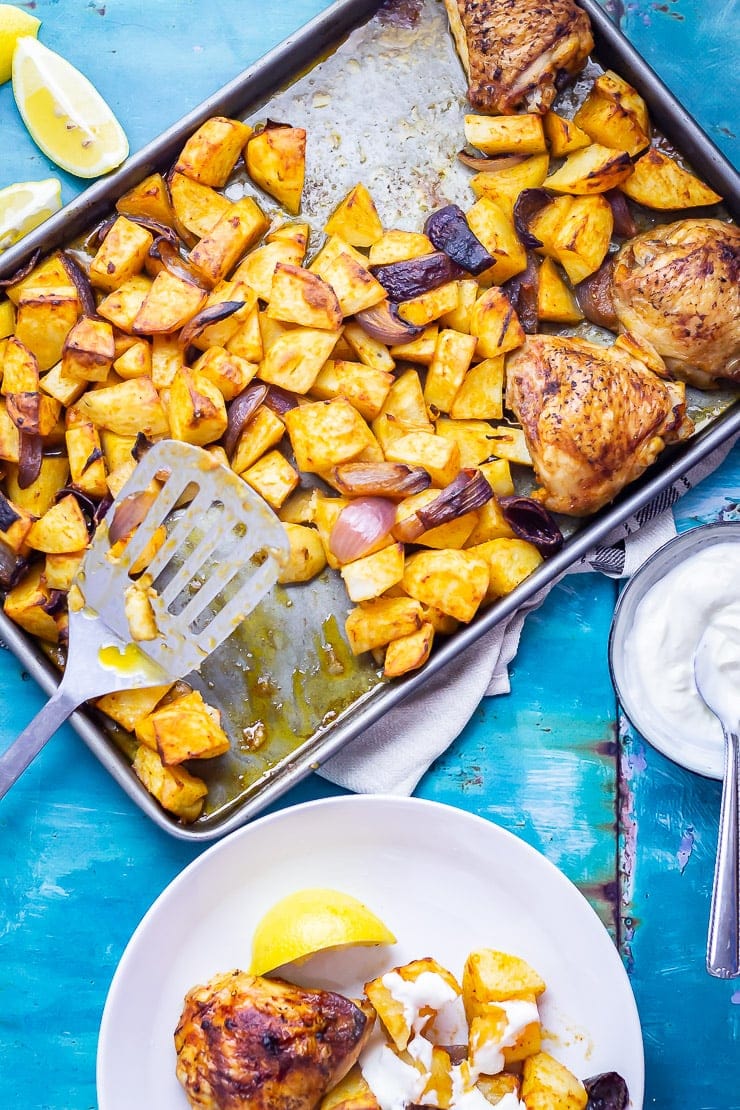 Overhead shot of Sheet Pan Harissa Chicken with Potatoes on a blue background with a white bowl