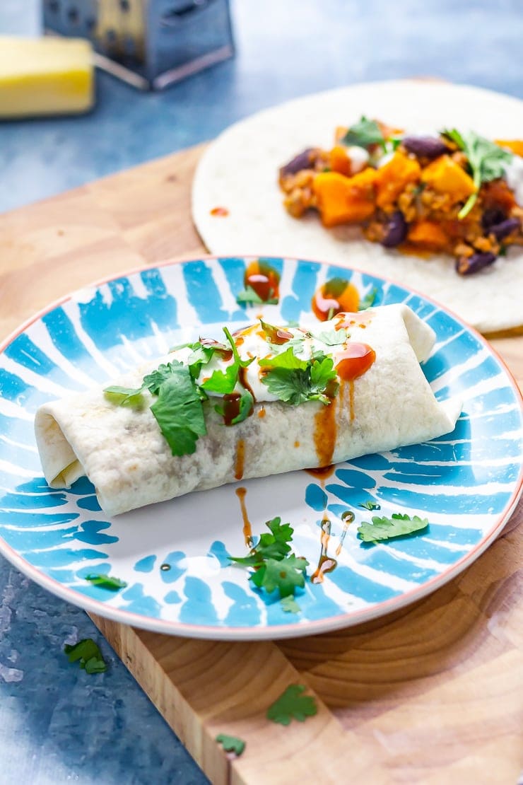 Burrito on a plate on a wooden board with an unrolled burrito in the background