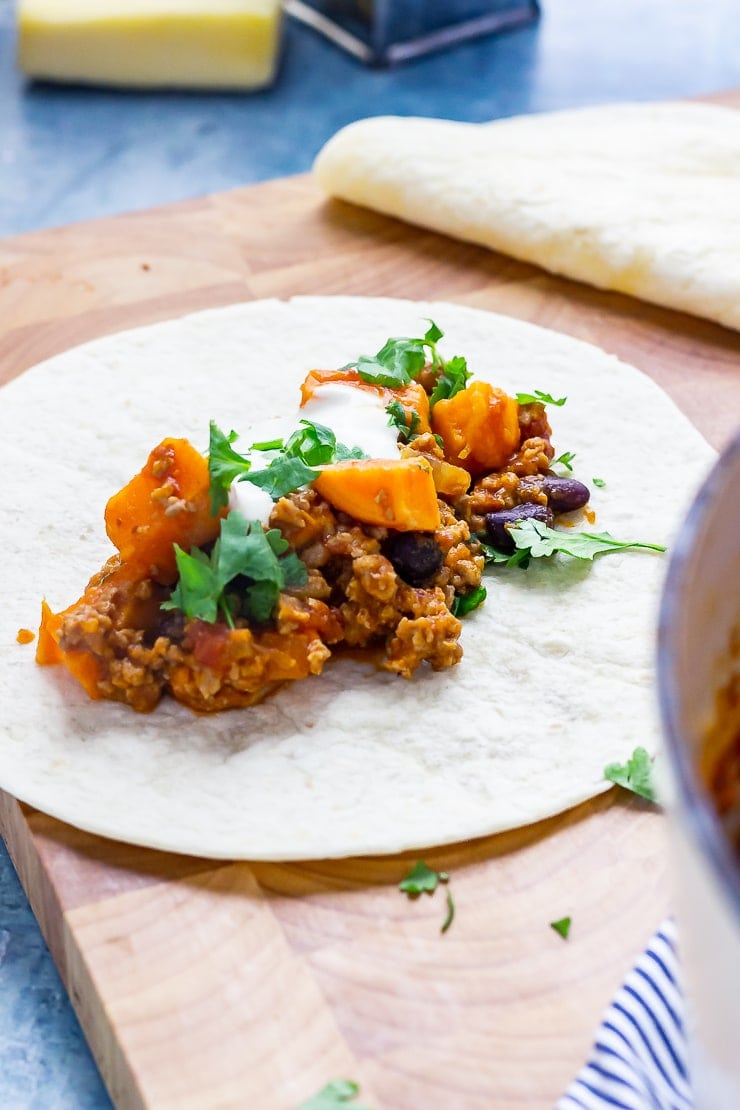 Turkey chilli burrito on a wooden board with cheese and grater in the background