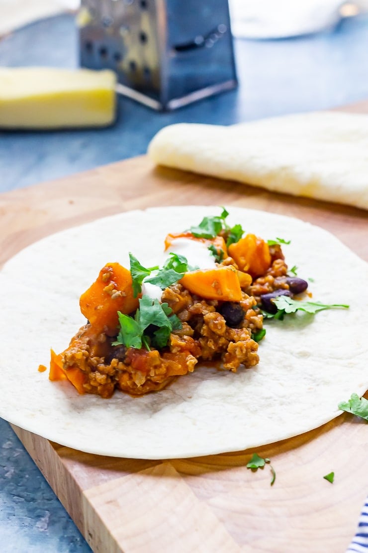 Turkey chilli burritos on a wooden board with cheese and a grater in the background