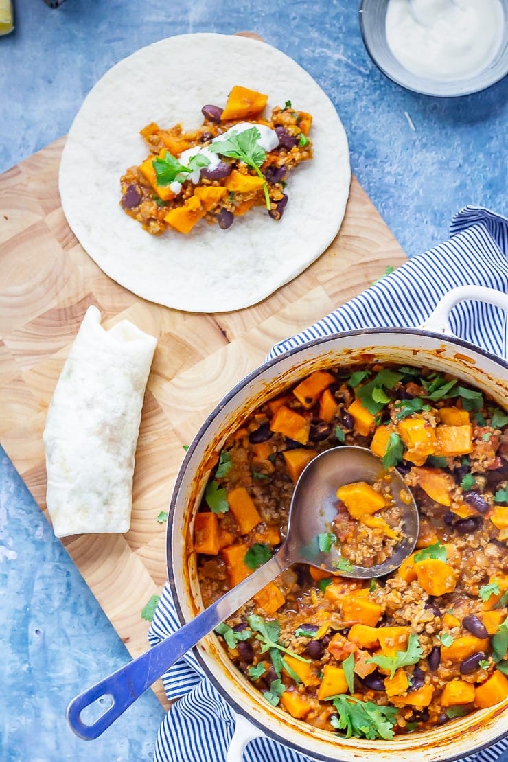 Overhead shot of Burritos with Chipotle Turkey & Sweet Potato Chilli on a wooden board and blue background