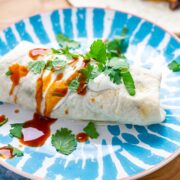 Turkey burrito on a plate with hot sauce on a wooden board